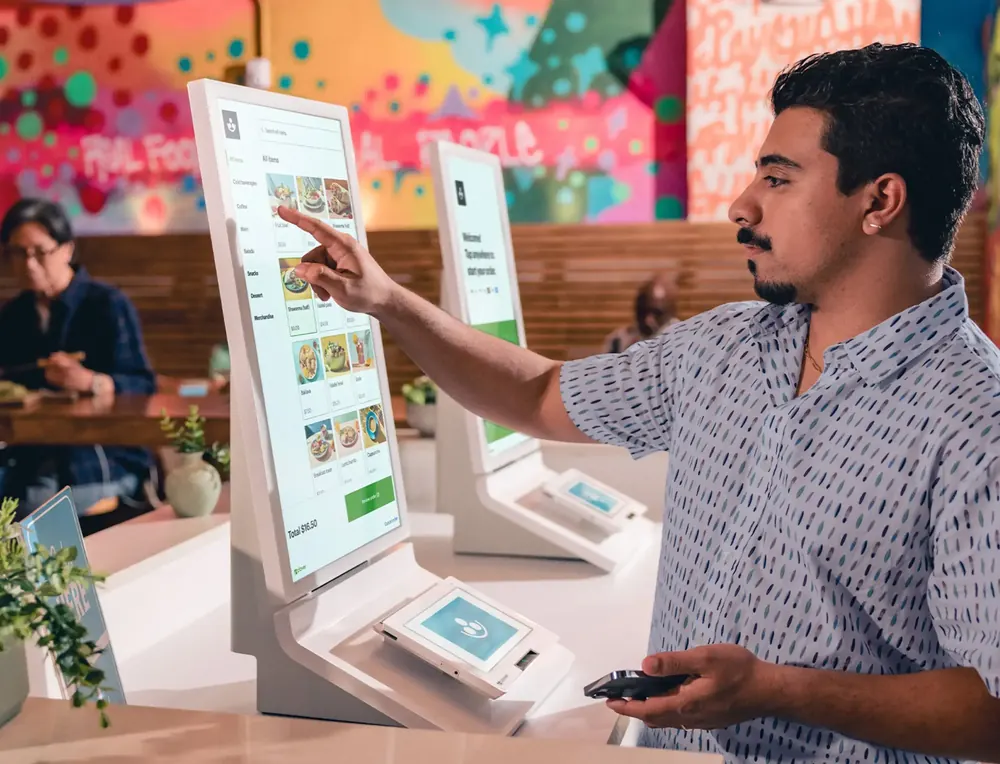 A customer ordering on a Clover Kiosk in a colorful restaurant