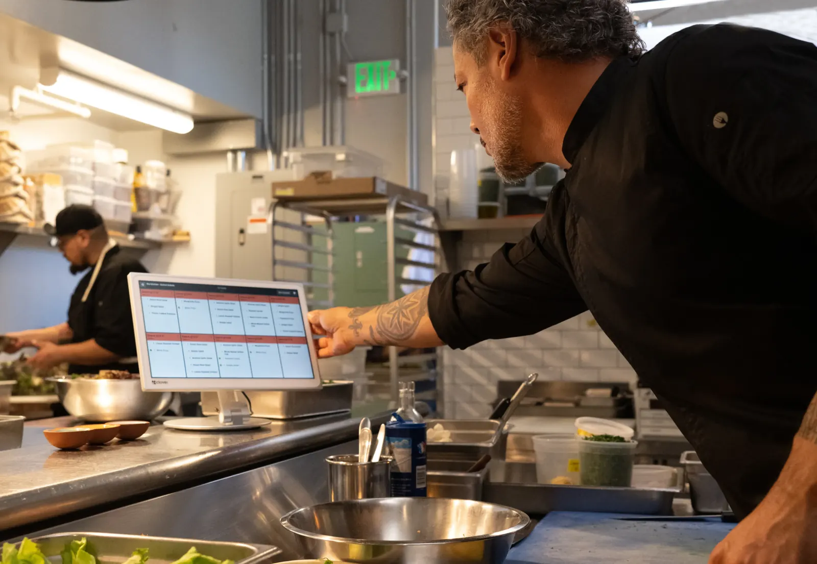 A chef checking orders on a Clover Kitchen Display in a busy restaurant kitchen