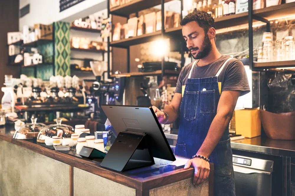 A barista ringing up an order on a Shift4 Dine workstation in a busy coffee shop