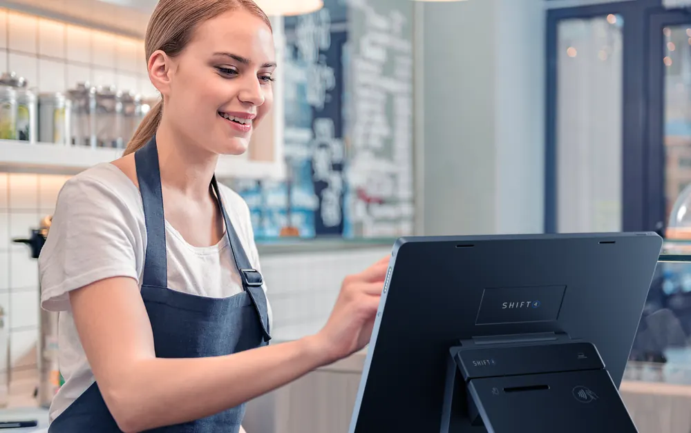 A cafe employee smiling while tapping the Shift4 Dine touchscreen
