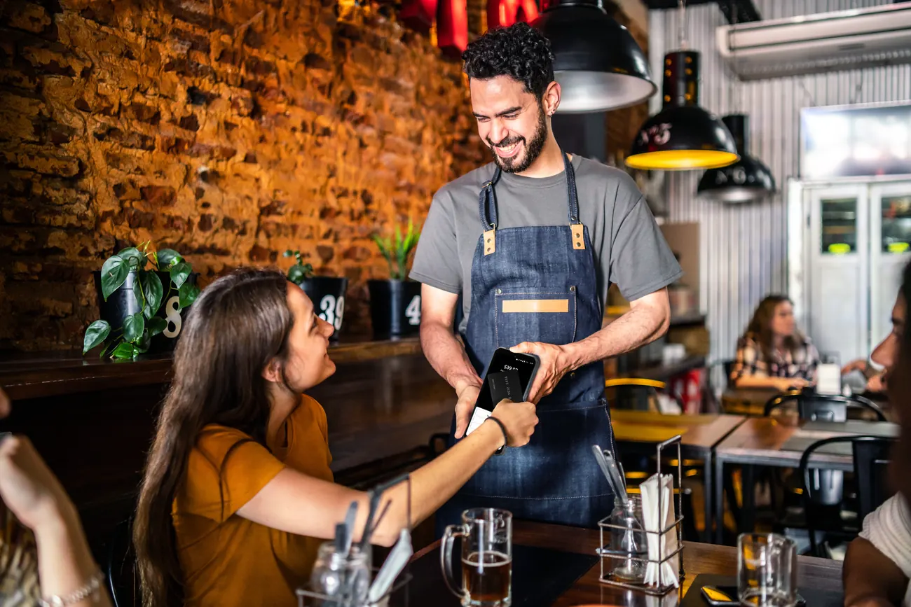 A server taking a guest's payment at the table with a Shift4 Dine handheld