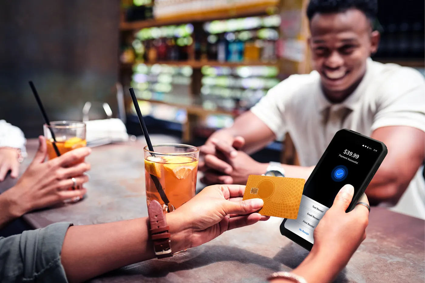 A smiling bartender holding a Shift4 Dine handheld while a guest taps their card to pay